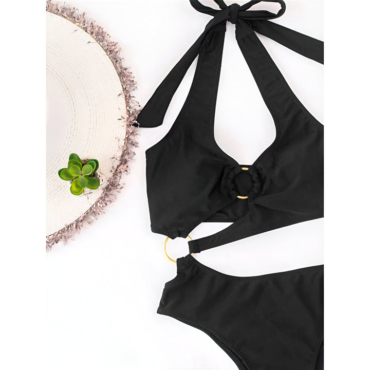 Une femme prenant un selfie dans un maillot de bain noir une pièce avec des détails dorés, portant des bijoux et du vernis à ongles noir.