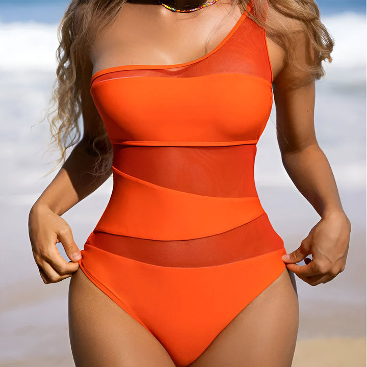 Image d'une femme portant un maillot de bain une pièce noir avec des empiècements en tulle transparent. Elle porte un collier coloré et a de longs cheveux blonds ondulés.