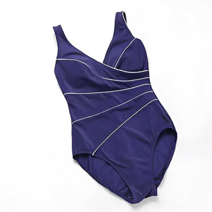 Une femme porte un maillot de bain une pièce vert émeraude avec des détails blancs croisés. Le maillot a un décolleté en V et des bretelles larges. La femme a les cheveux courts et bruns.