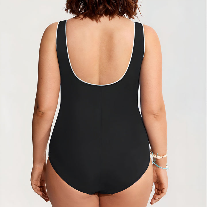 Femme portant un maillot de bain une pièce bleu marine avec des rayures blanches, collier de perles et bracelet. Style élégant et confortable pour la plage ou la piscine.