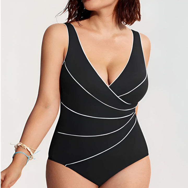 Maillot de bain 1 pièce prune avec des liserés blancs, col en V croisé. Femme portant un collier de perles et un bracelet beige. Idéal pour la plage ou la piscine.