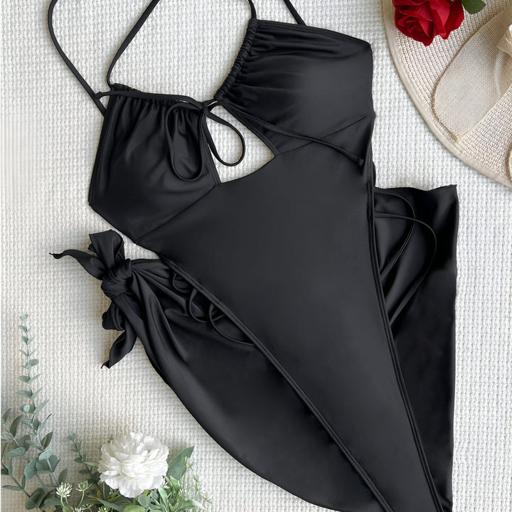 Image d'une femme portant un maillot de bain vert fluo une pièce avec des détails lacés et un paréo court à imprimé serpent vert et noir noué à la taille. Le fond est un mur en pierre claire.