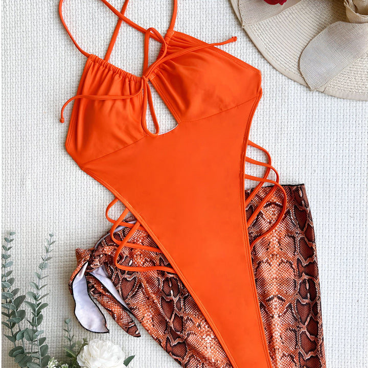 Image d'une femme portant un maillot de bain une pièce noir avec découpes et une jupette noire. La tenue met en valeur sa silhouette et est accessoirisée d'un collier discret.