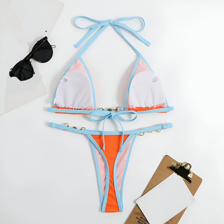 Image d'un bikini tendance orange et bleu avec des détails de perles, posé à plat avec des lunettes de soleil et un presse-papier, évoquant un style estival et chic pour la plage.
