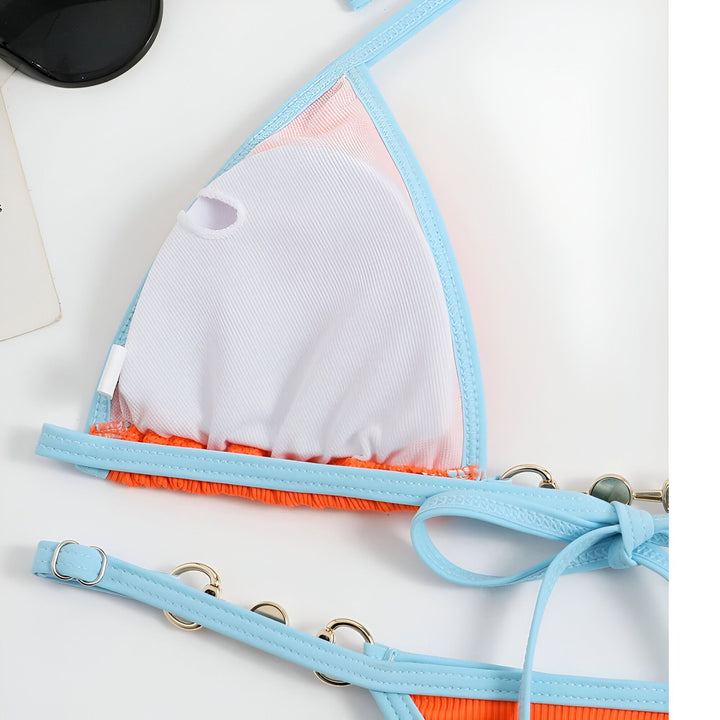 Vue arrière d'une femme blonde portant un bikini orange et turquoise sur une plage ensoleillée avec des palmiers.