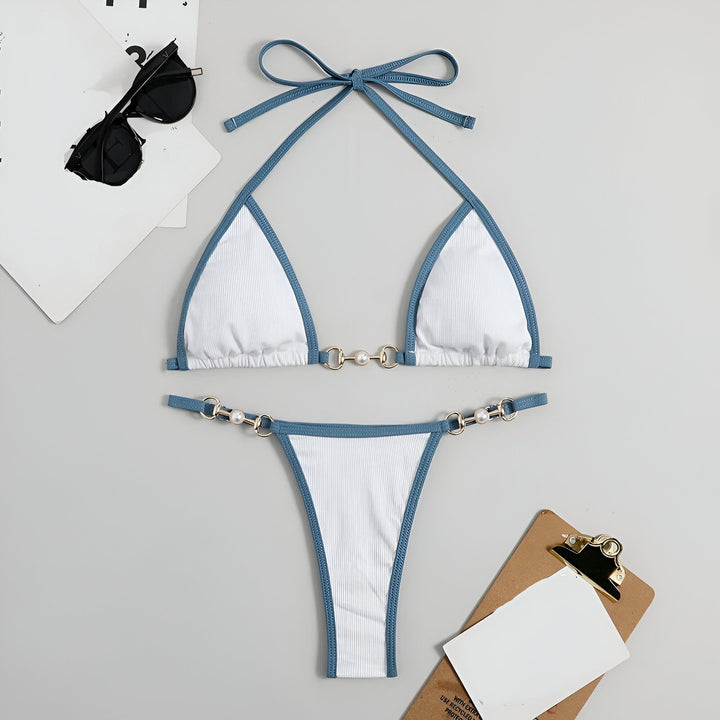 Femme en bikini rose et vert sur une plage ensoleillée, eau turquoise en arrière-plan. Maillot de bain tendance avec détails dorés. Vacances d'été, mode balnéaire.