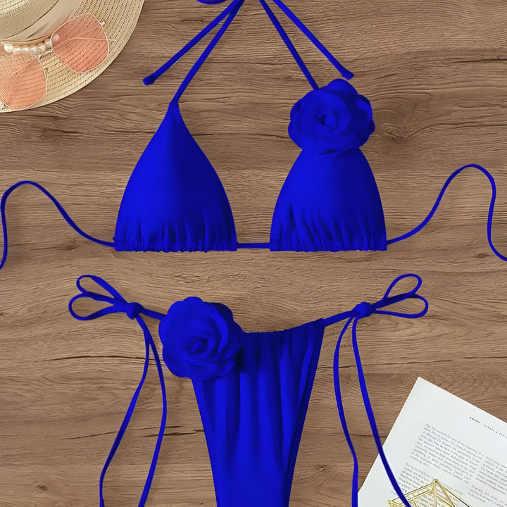Vue rapprochée d'un bikini bleu vif avec des détails de fleurs, un chapeau de paille et des lunettes de soleil. Idéal pour la plage ou la piscine.