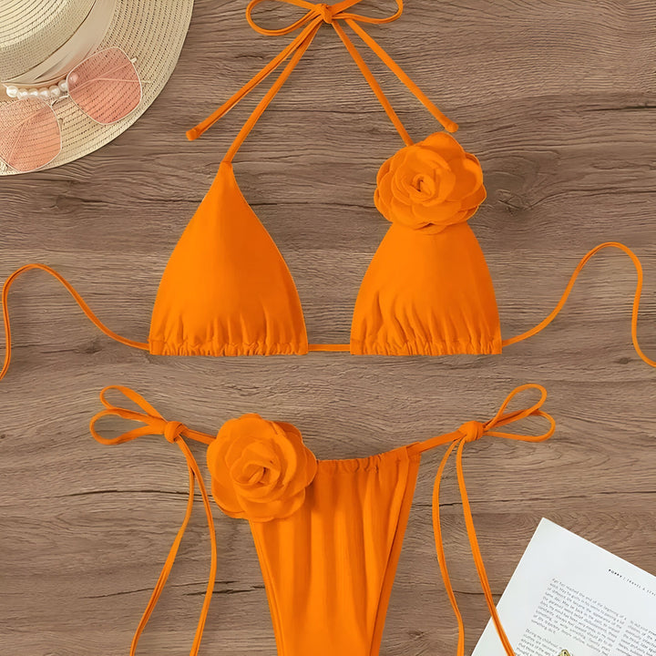 Maillot de bain orange à fleurs avec chapeau et lunettes de soleil roses sur un fond en bois. Ensemble de bikini triangle avec ornements floraux. Idéal pour la plage ou la piscine. Mode estivale tendance.