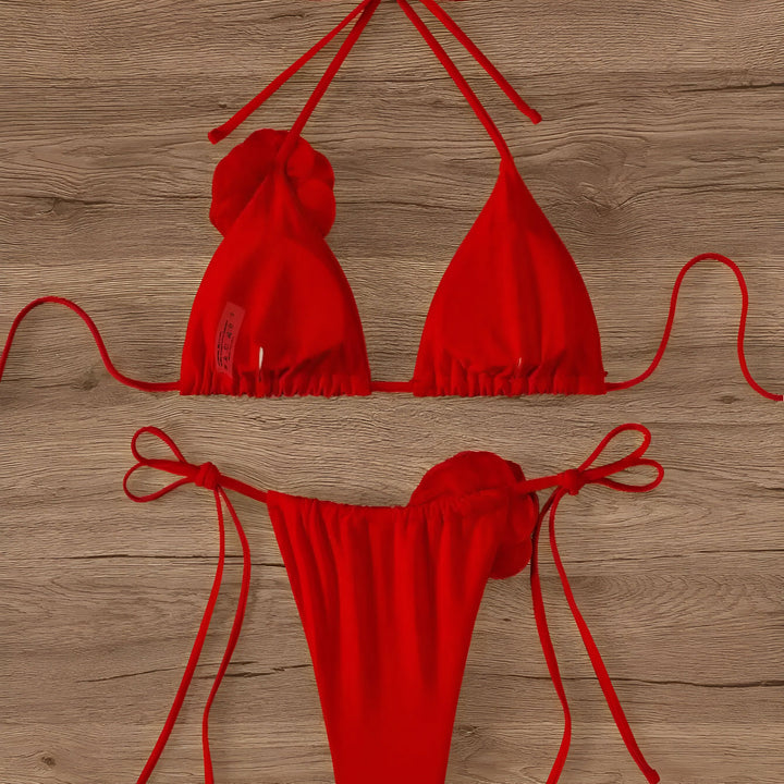 Ensemble de bikini rose vif avec détails de roses, posé sur une table en bois. Chapeau de paille et lunettes de soleil à proximité. Ambiance estivale et tendance. Idéal pour la plage ou la piscine. Prêt pour les vacances!