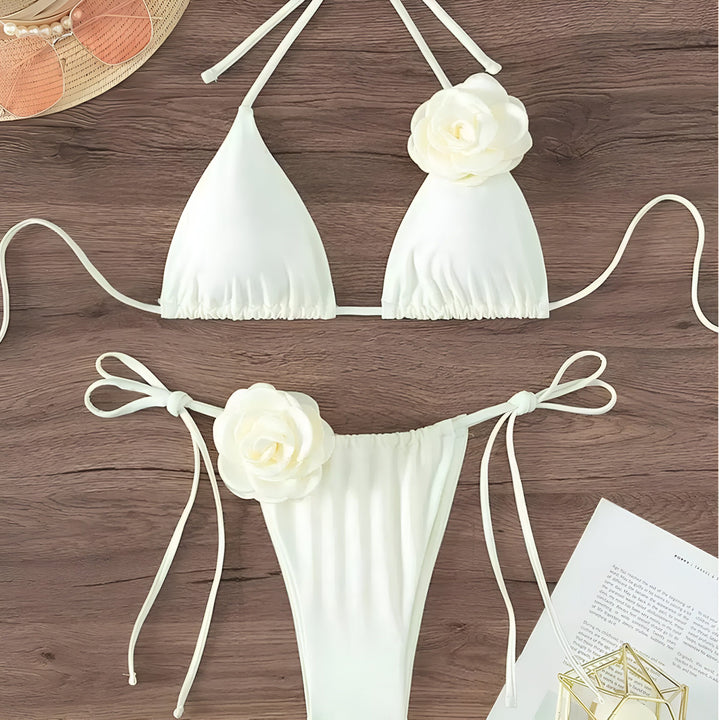 Vue de dessus d'un bikini noir avec des détails floraux, un chapeau de paille, des lunettes de soleil roses et un magazine sur une table en bois. Style estival, mode féminine.