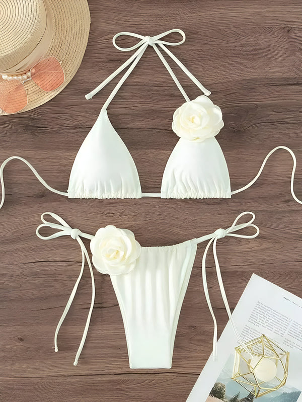 Gros plan d'un bikini blanc avec détail de fleur, mis en valeur sur un fond de bois texturé. Conception élégante et raffinée, idéale pour une escapade à la plage.
