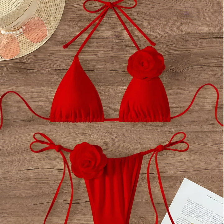 Maillot de bain rouge deux pièces avec fleurs décoratives, lunettes de soleil roses, chapeau de paille et magazine sur une table en bois. Style d'été, mode plage.