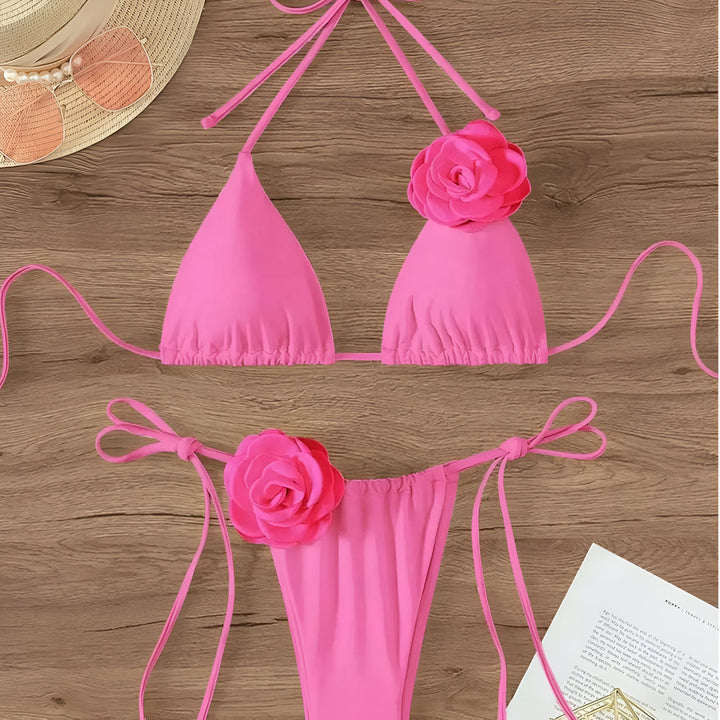 Maillot de bain noir deux pièces avec fleurs, lunettes de soleil roses et chapeau de paille sur une table en bois. Idéal pour l'été et la plage !