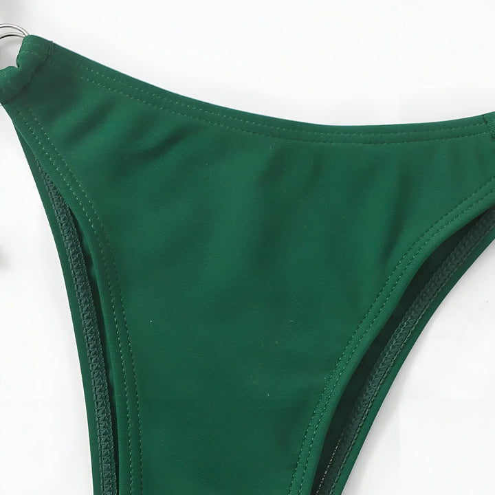 Femme en bikini lilas avec collier Afrique, assise sur un canapé. Maillot de bain deux pièces noué, mode été, vacances à la plage. Bijou doré, silhouette mince, bronzage parfait. Style estival.