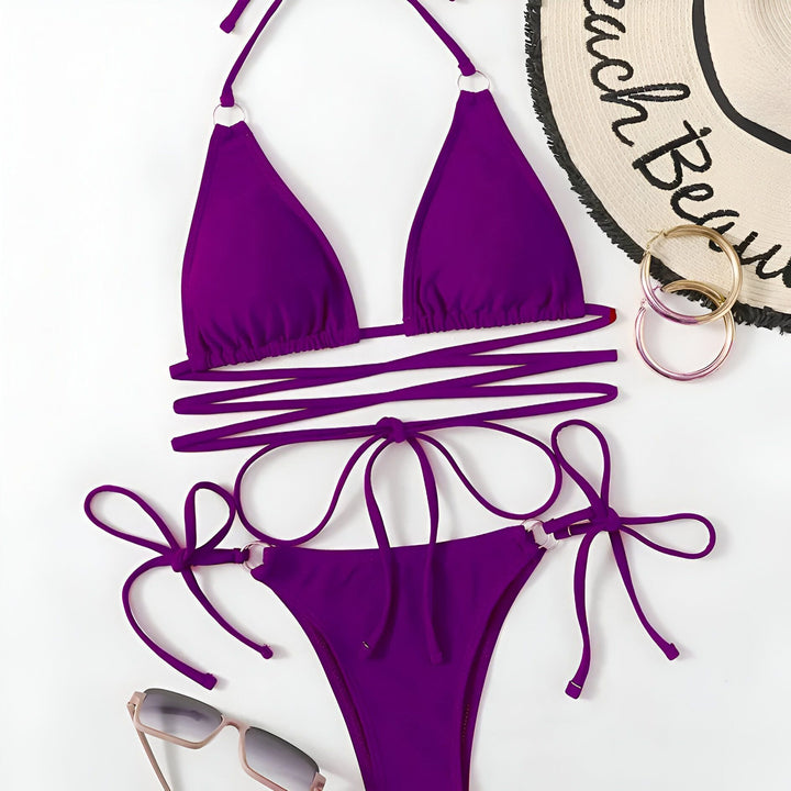 Femme en bikini rose vif. Le bikini a des anneaux métalliques et des cordons qui s'enroulent autour de la taille. Elle porte un collier doré avec un pendentif en forme d'Afrique.