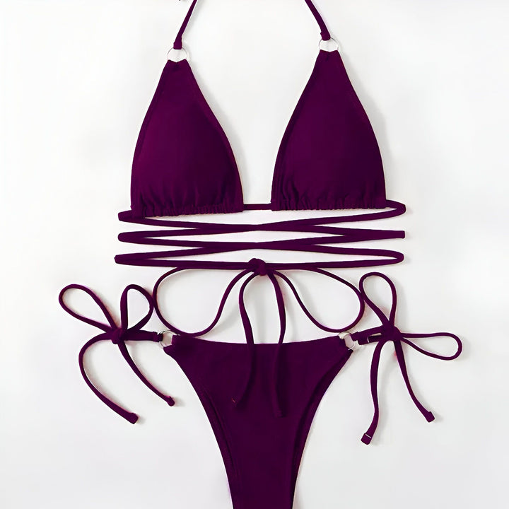 Femme portant un bikini vert avec des liens croisés, mains sur les hanches, posant devant un mur blanc. Mode de plage, maillot de bain, style estival.