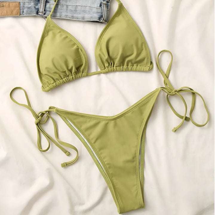 Femme en bikini bleu électrique avec des liens croisés. Elle porte un collier avec un pendentif en forme d'Afrique. Assise sur un canapé gris.