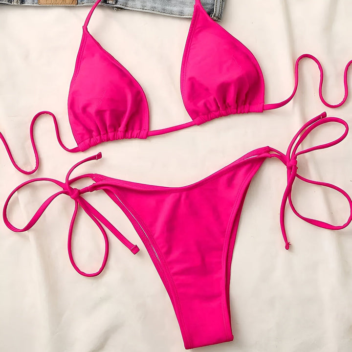 Image d'une femme portant un bikini noir avec des lanières croisées autour de la taille. Elle porte un collier avec un pendentif rectangulaire. Elle a des ongles avec une manucure française.