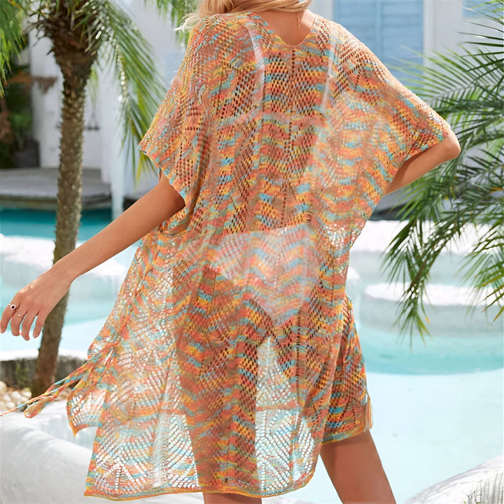 Femme blonde avec un chapeau et une tunique de plage colorée, tenant un sac de paille. Piscine et palmier en arrière-plan. Look estival et décontracté pour les vacances.