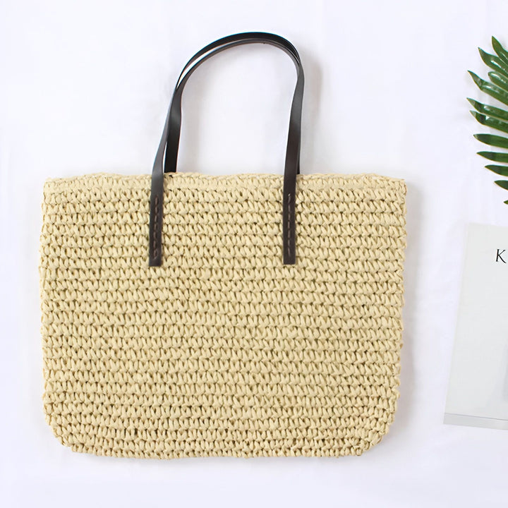 Femme portant un sac en paille avec des anses en cuir marron, robe bleue et bracelet turquoise. Manucure verte.