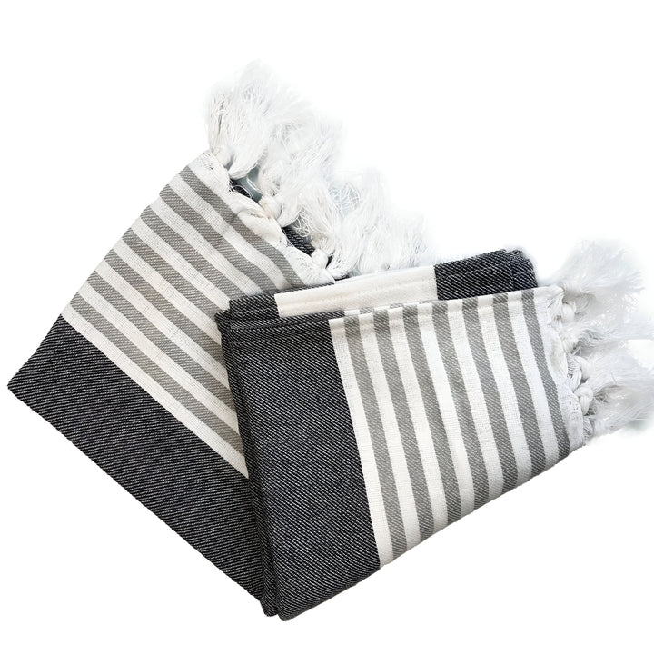 Serviette de plage rayée grise et blanche, avec des franges blanches sur les bords, vue de dessus sur fond blanc.
