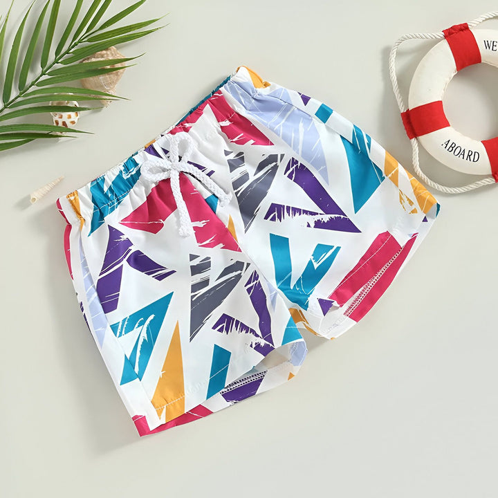 Short de bain pour enfant avec motifs géométriques colorés. Cordon blanc à la taille. Décor nautique avec bouée de sauvetage et coquillages. Idéal pour la plage et la piscine.