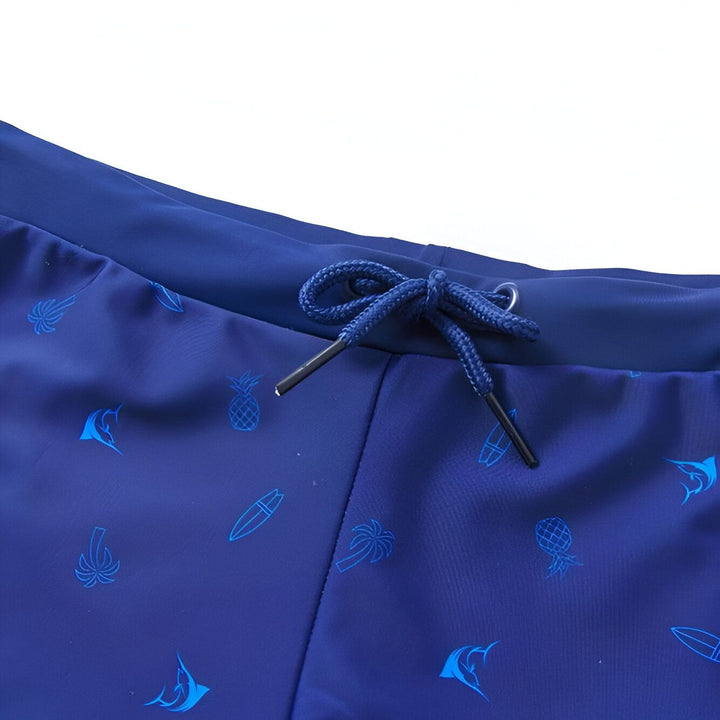 Short de bain bleu marine à motifs de poissons, ananas et palmiers, décoré d'étoiles de mer, d'une feuille de palmier et d'un coquillage.