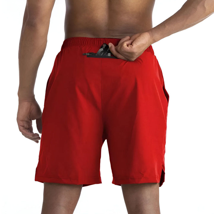 Homme torse nu portant un short de bain bleu marine avec une poche zippée à l'arrière. Vue de dos sur fond blanc.