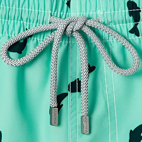 Vue rapprochée d'un short de bain turquoise à motifs de baleines noires, avec une doublure intérieure blanche visible. Le short a une poche latérale et une taille élastique. Idéal pour la plage ou la piscine.