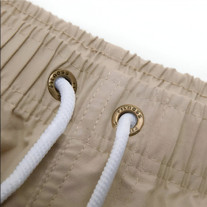 Vue arrière d'un homme torse nu en short de bain turquoise. Le bras gauche est tatoué.