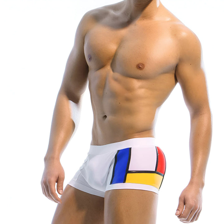 Homme torse nu en slip de bain blanc avec bloc de couleurs bleu et jaune, éclairage studio lumineux.