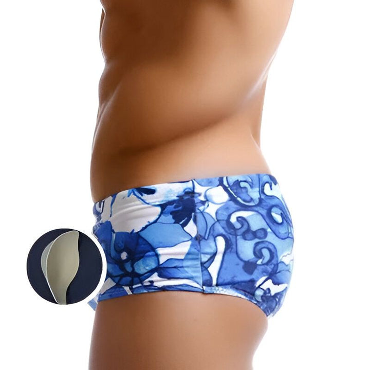 Torse d'homme avec abdominaux dessinés, portant un slip de bain bleu et blanc à motifs floraux. Mode masculine, été, plage.