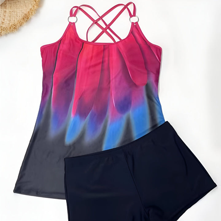 Maillot de bain deux pièces pour femme : haut tankini imprimé dégradé rose, bleu et noir, et short de bain noir. Chapeau de paille en arrière-plan.