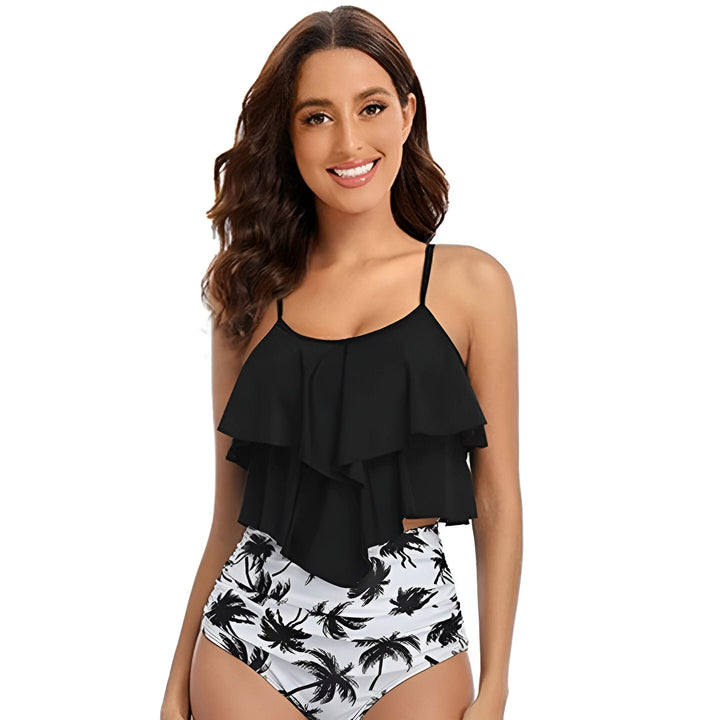 Femme souriante portant un maillot de bain deux pièces. Le haut est noir à volants et le bas est taille haute avec un motif de palmiers noir et blanc.