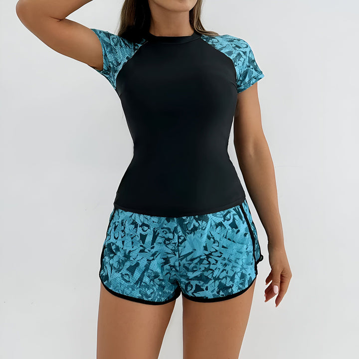 Femme portant un ensemble de sport : haut noir à manches courtes et short bleu turquoise à motifs. Idéal pour l'entraînement ou la détente.